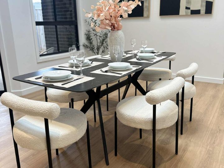A bright dining table set with white chairs and a floral vase, showcasing a stylish home staging design.